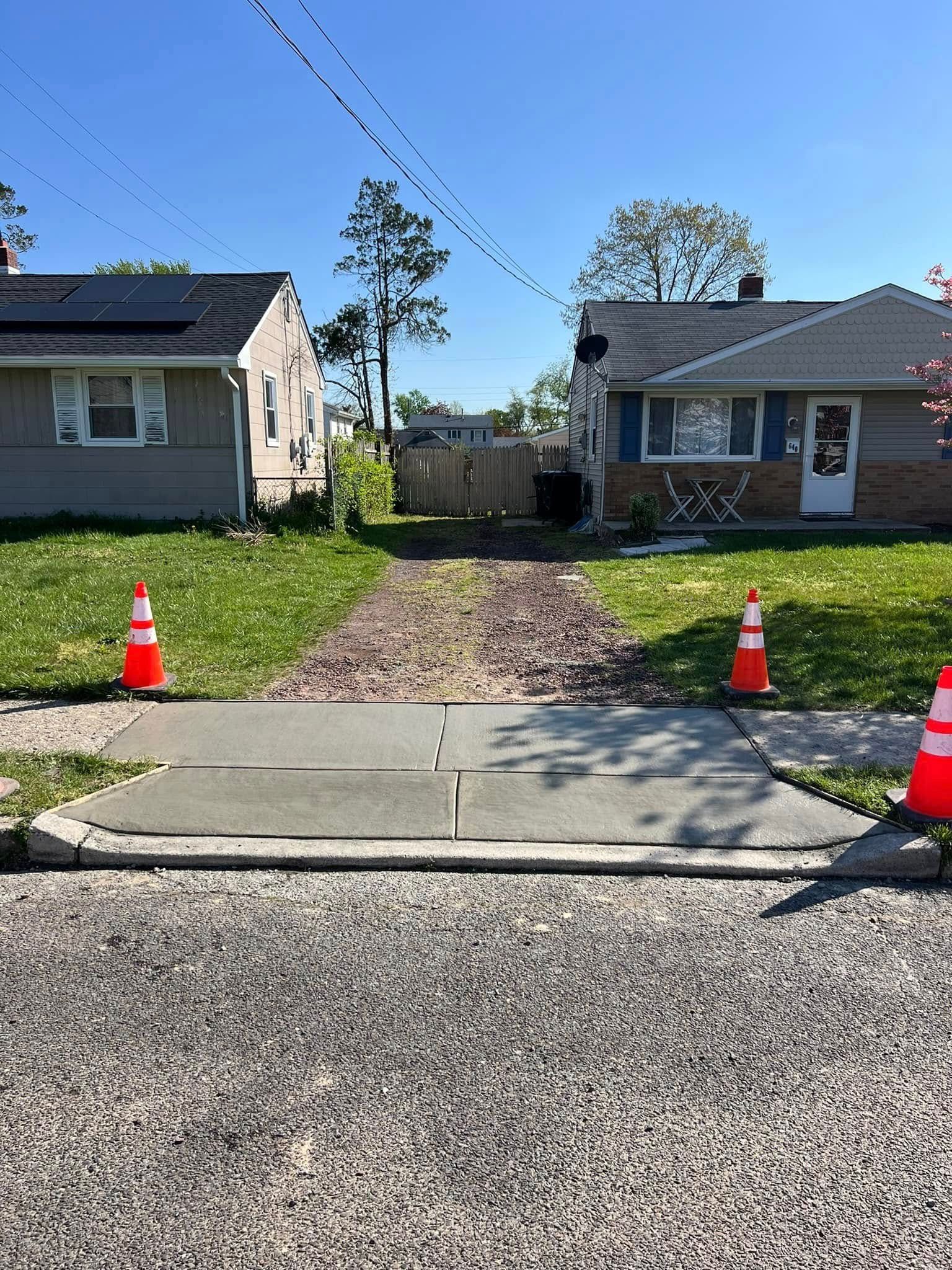 Concrete sidewalk with orange cones, leading to a gravel path between two houses.