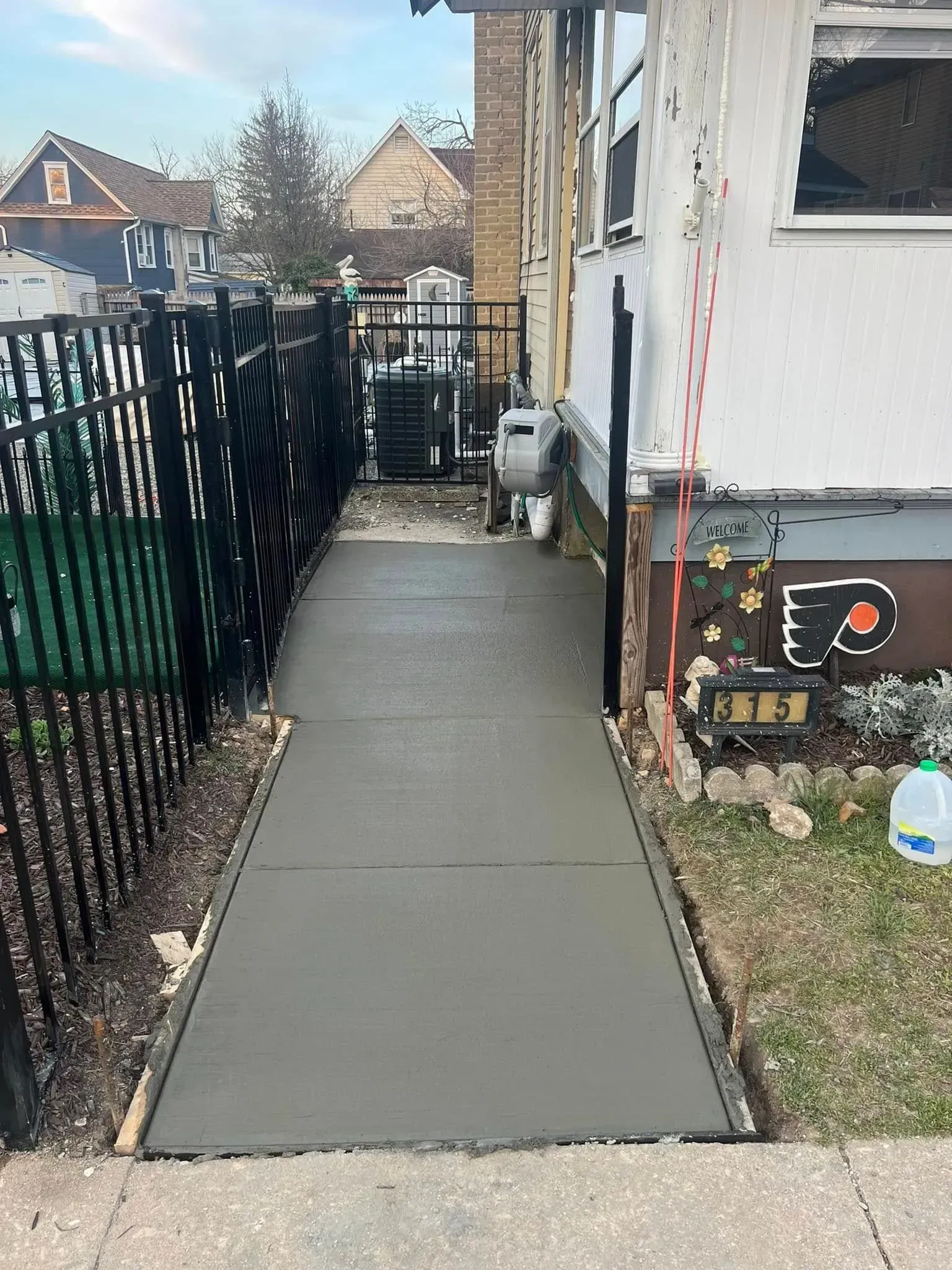 Freshly poured concrete sidewalk next to a black fence and a house with a Flyers logo.