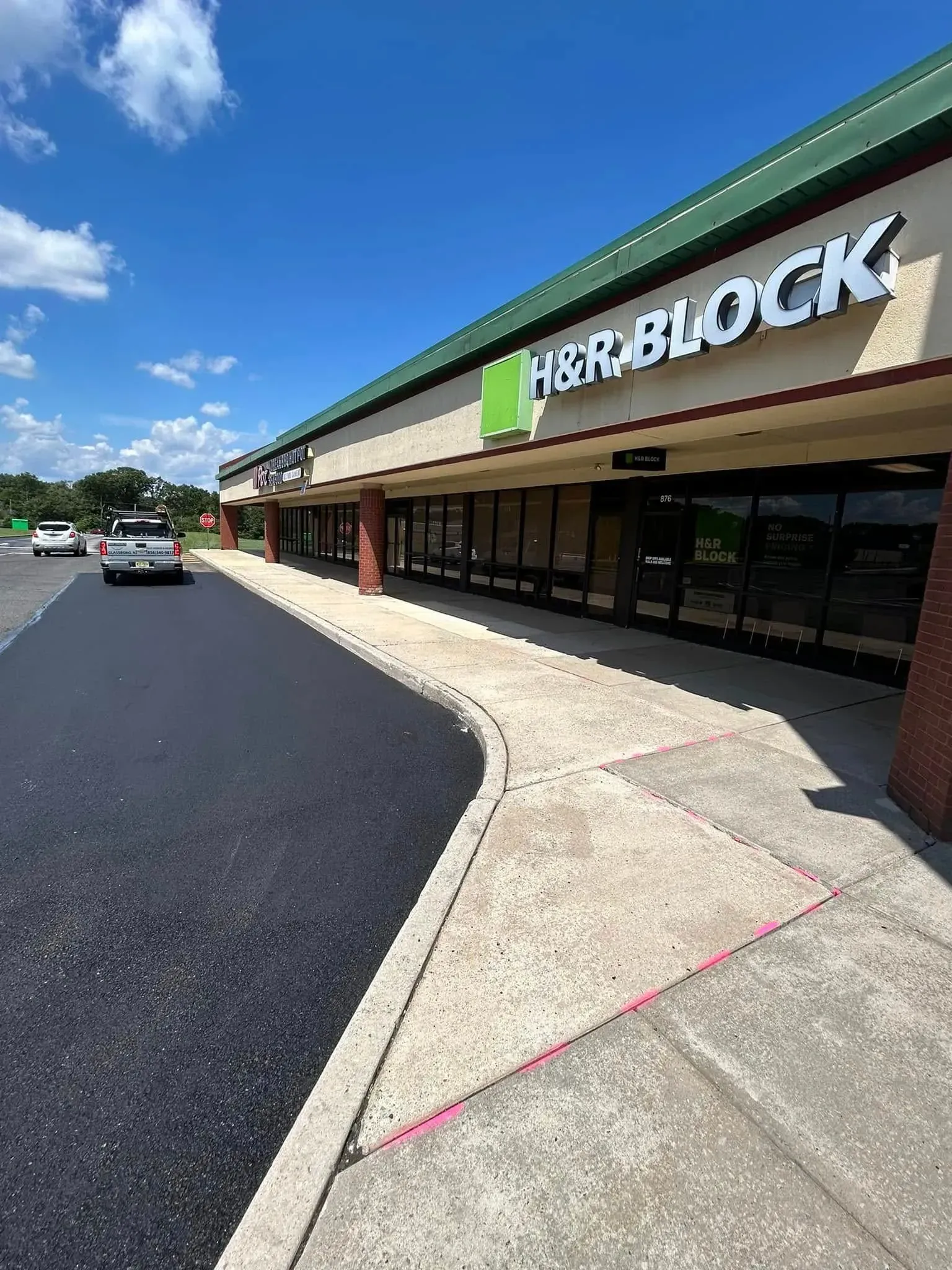 H&R Block storefront with a newly paved parking area. A car is driving down the street on a sunny day.