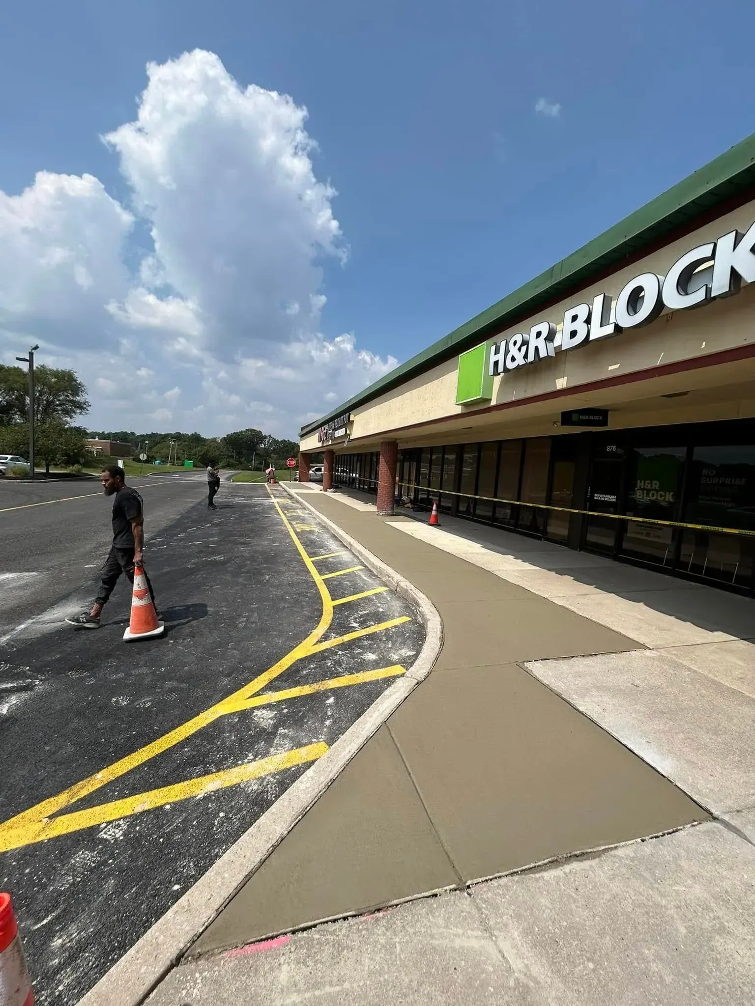 Sidewalk construction at an H&R Block. Workers near fresh concrete on a sunny day.