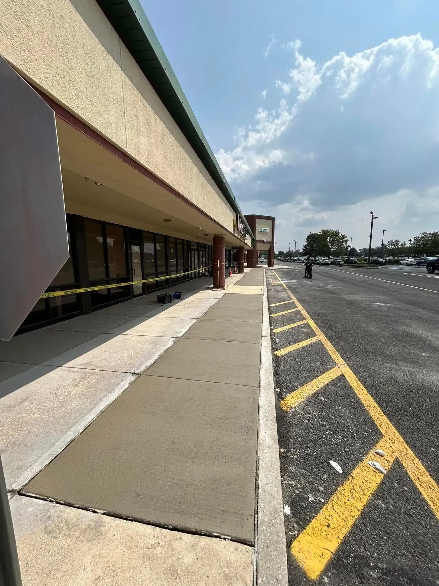 Sidewalk in front of a strip mall with yellow parking lines; cloudy sky.