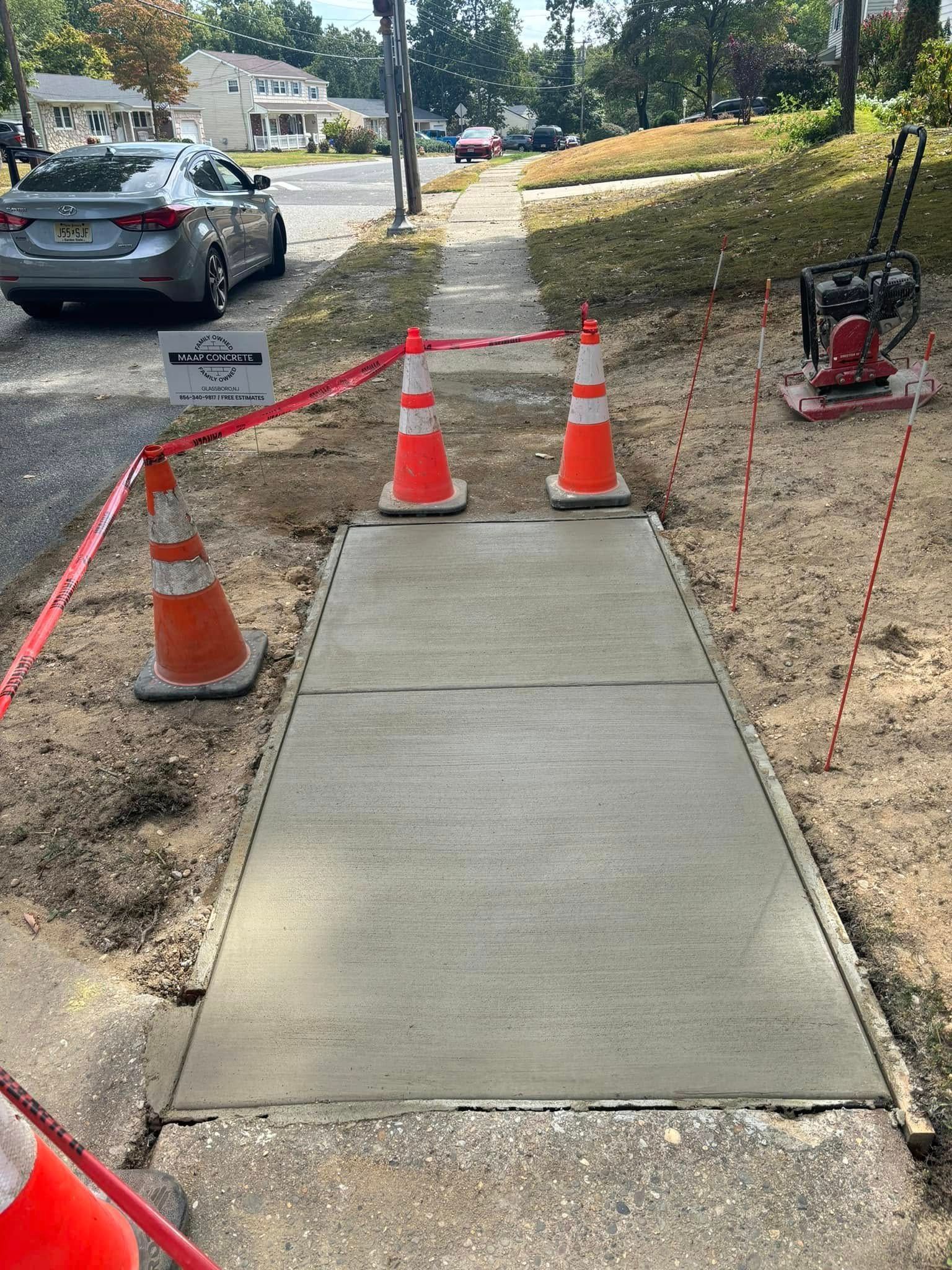 Newly poured concrete sidewalk blocked by orange cones and caution tape.