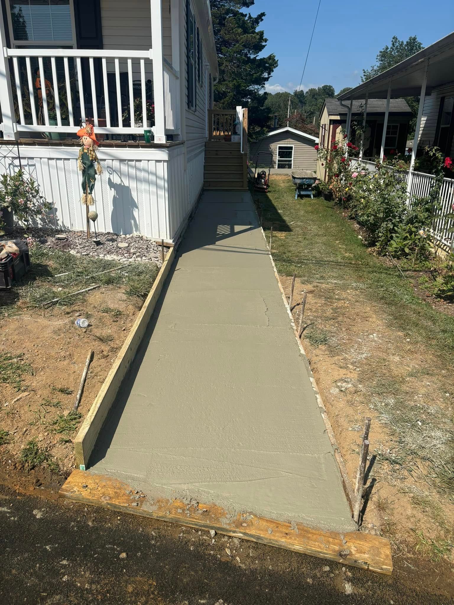 Newly poured concrete walkway leading to a house with wooden stairs.