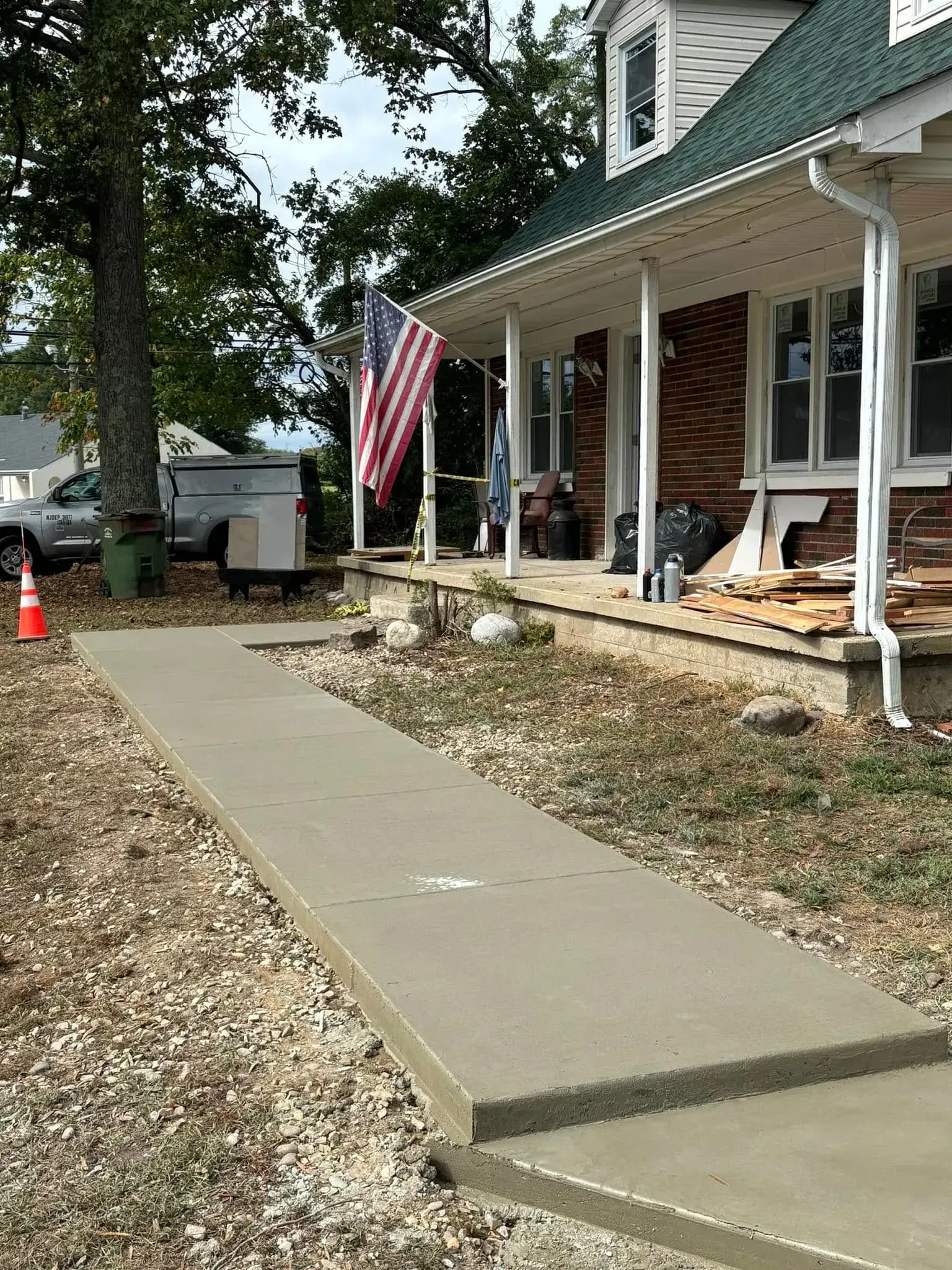 A newly poured concrete walkway leads to a house with a porch. American flag flies.