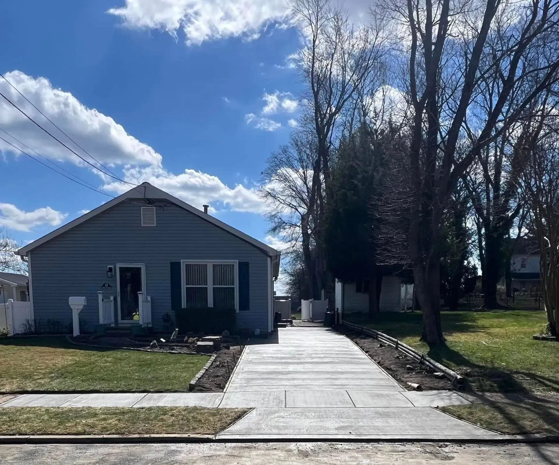 A blue house with a concrete driveway under a partly cloudy sky.