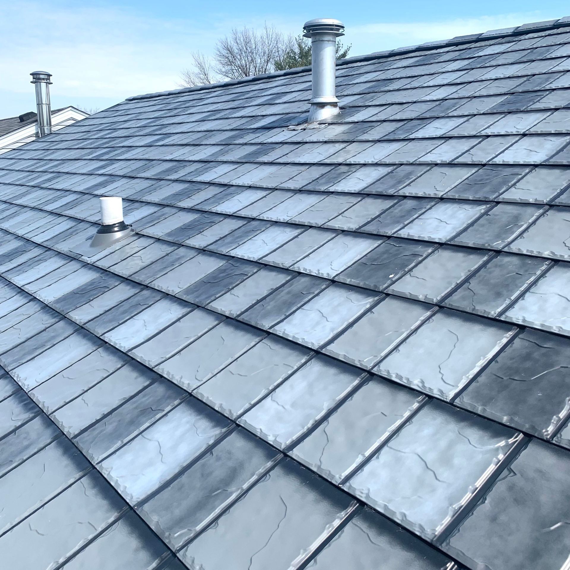 Gray slate tile roof with three silver vent pipes.