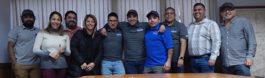 A group of people posing in front of a window. Some have arms around each other.