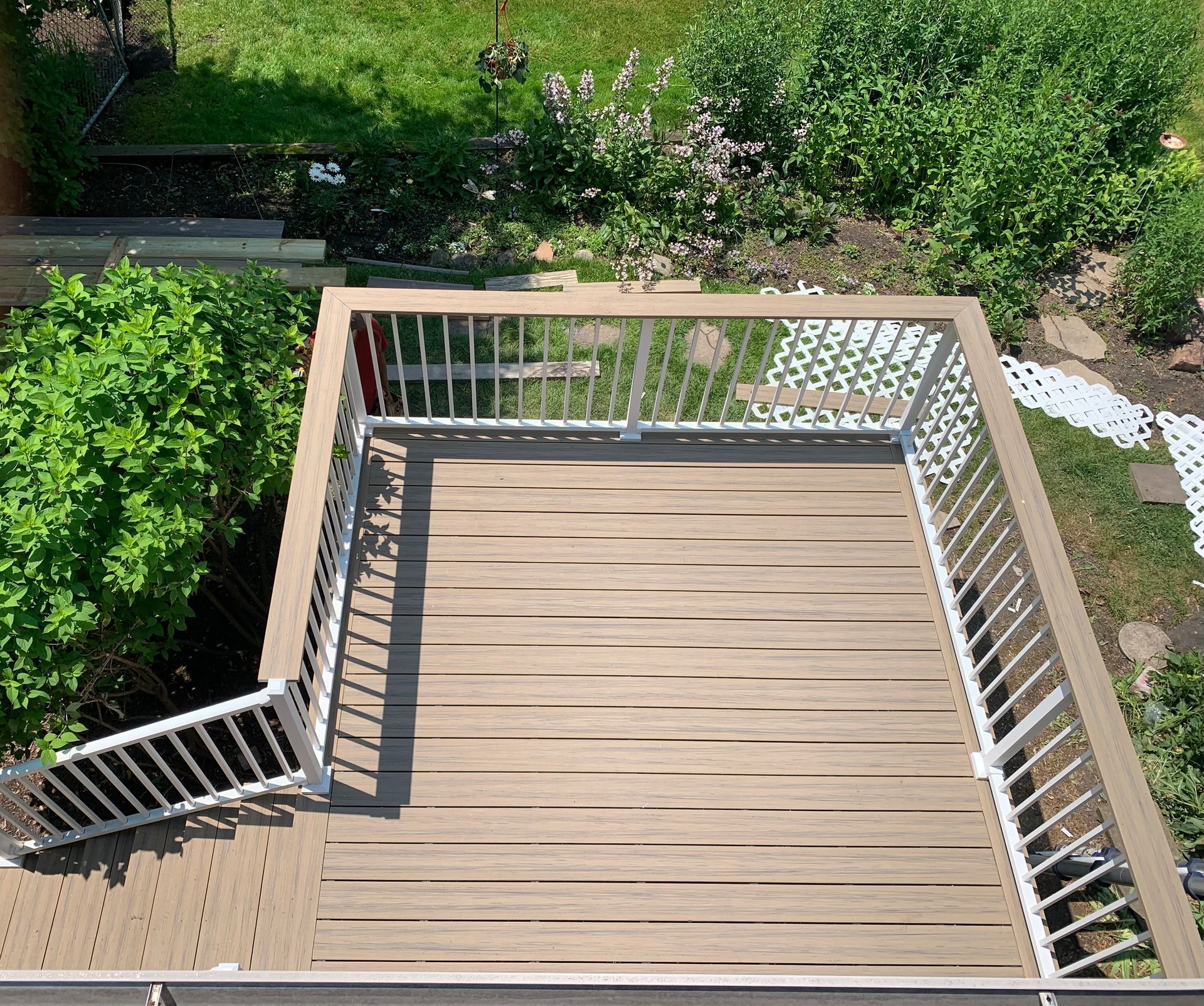 An elevated wooden deck with white railings, looking down onto a lush green backyard garden.
