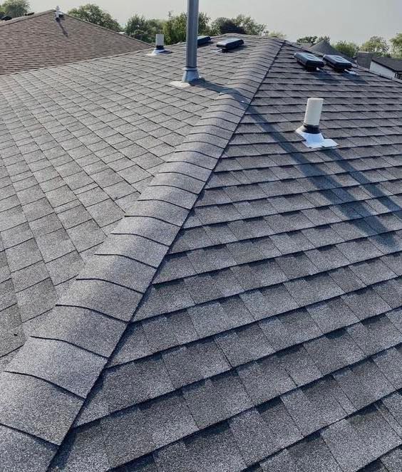 Person using a nail gun to install asphalt roof shingles on a rooftop.