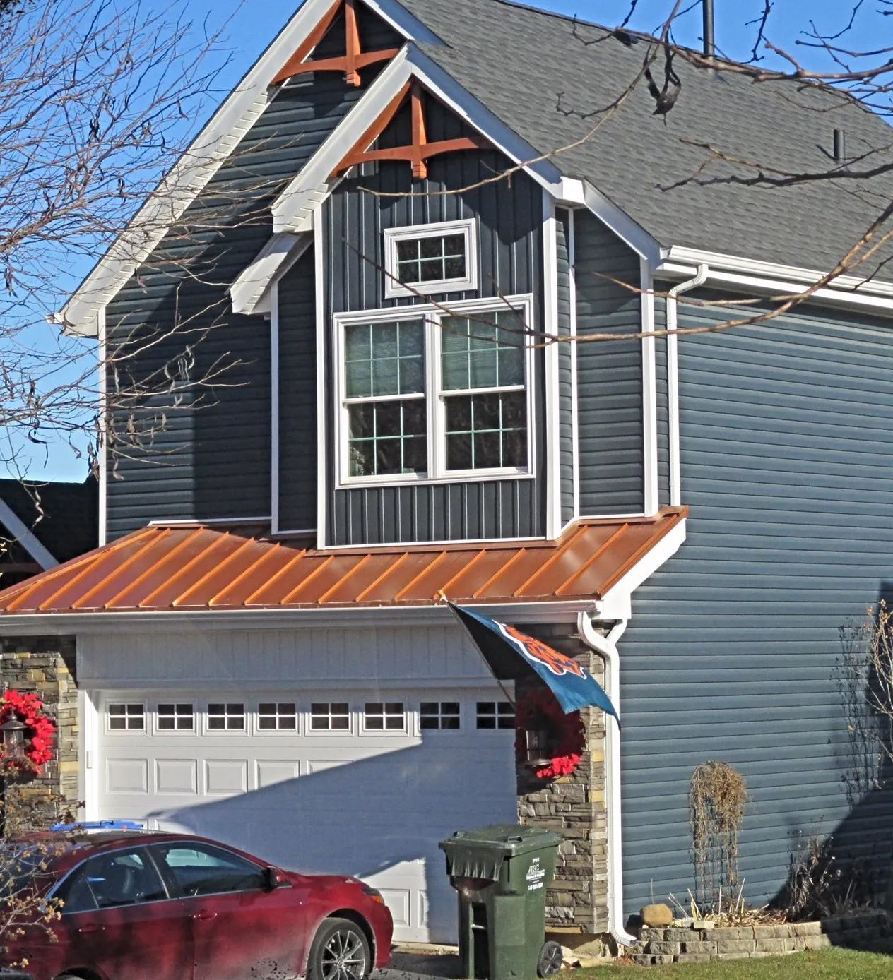 A two-story dark blue house with a copper-colored garage roof, a small top window, and a red car parked in the driveway.