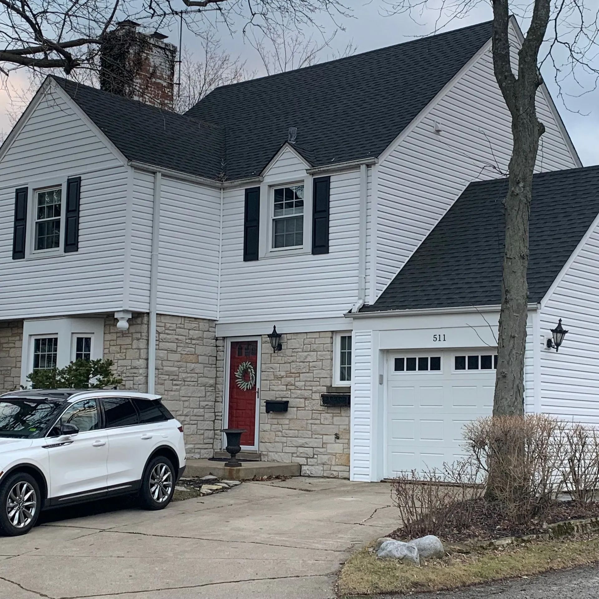A two-story house with white siding and stone accents, a black roof, a red front door, and an attached garage.