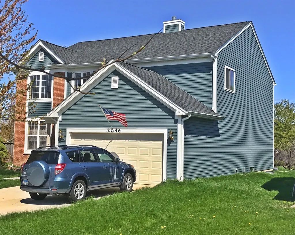 A blue two-story house with a tan garage door, a front-facing gable, and a blue SUV parked in the driveway.