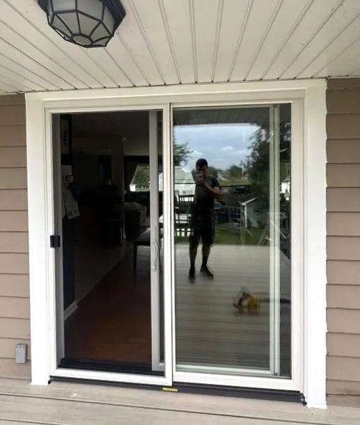 A sliding glass door on a house exterior, reflecting a person holding a camera on a wooden deck.