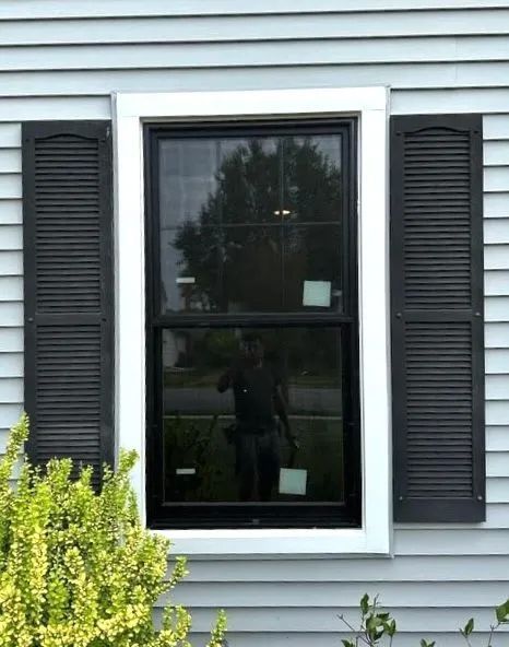 A single-hung window with a black frame and white trim, flanked by black shutters on light blue horizontal siding.