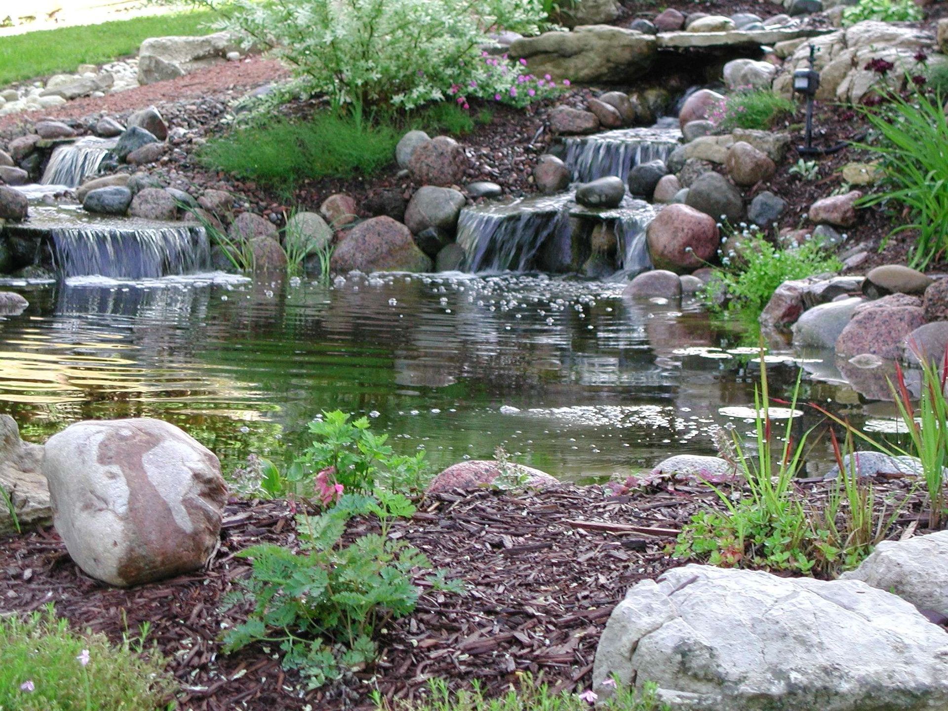 There is a waterfall in the middle of a pond surrounded by rocks.