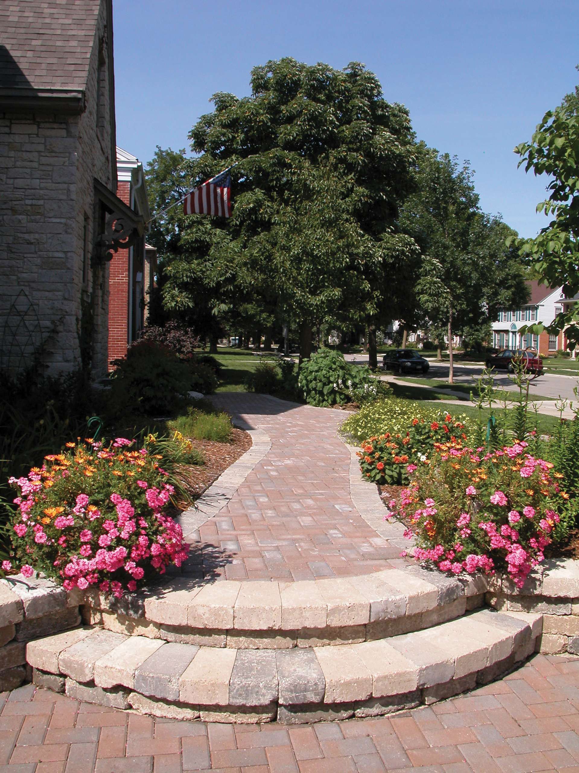 A brick walkway leads to a house with pink flowers.