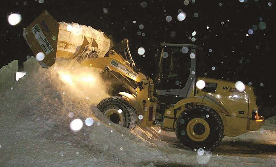 A bulldozer is clearing snow from a parking lot at night.