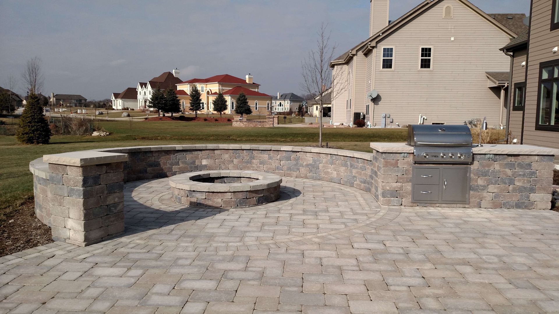 A brick patio with a fire pit and a grill.