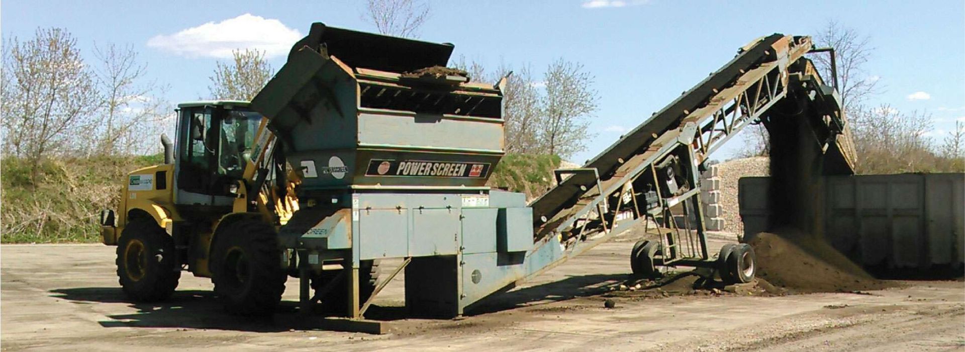 A yellow dump truck is driving through a dirt field.
