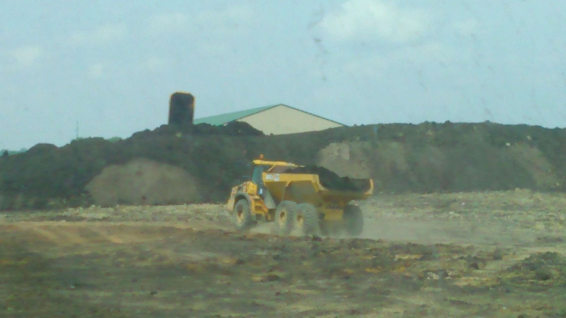 A yellow dump truck is driving through a dirt field.