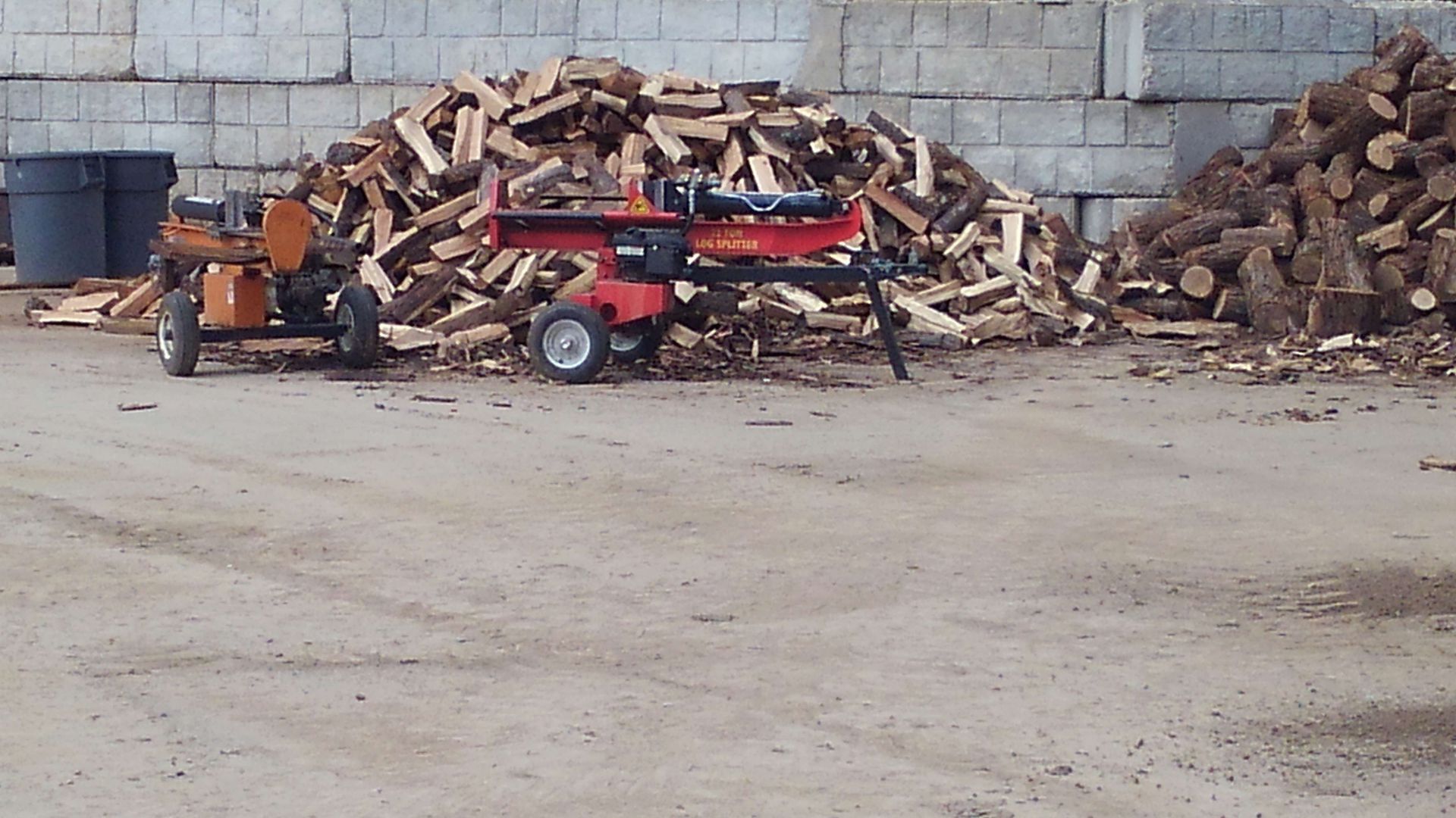 A red log splitter is sitting in front of a pile of logs