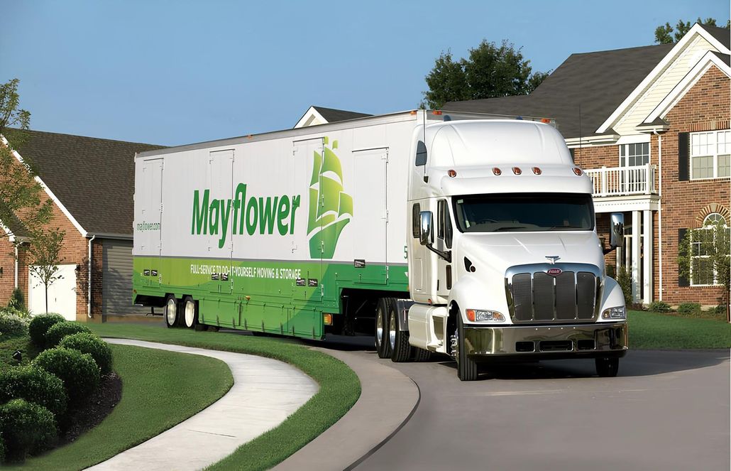 White Mayflower moving truck driving through a suburban neighborhood on a curved road.