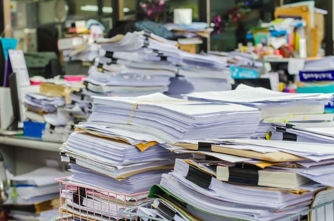 Stacks of papers and notebooks piled high on a cluttered office desk
