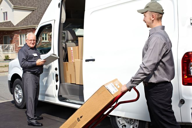 Delivery worker unloading a package from a white van while another man stands in the open doorway.