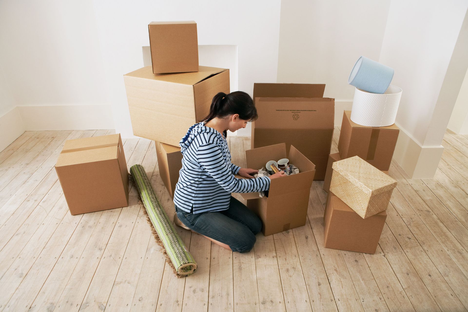 Person kneeling among cardboard boxes, packing belongings in a bright empty room