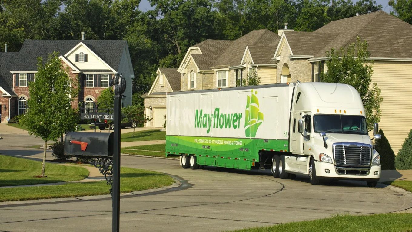 Mayflower moving truck on a suburban street with houses and trees in the background