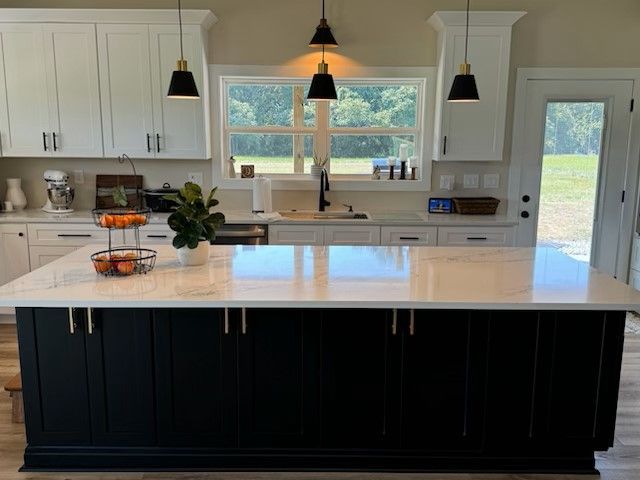 Modern kitchen with a black island, white countertops, cabinets, and pendant lights.