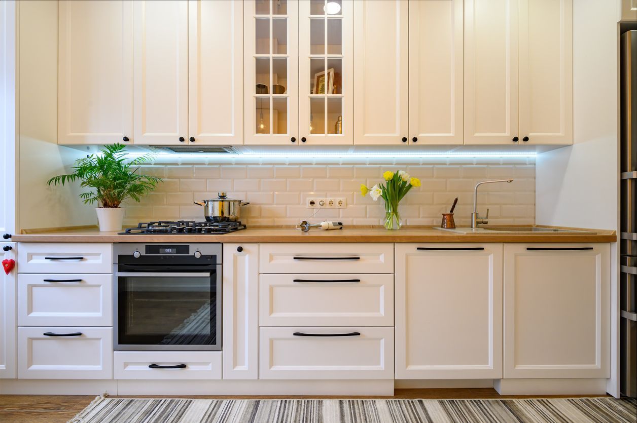 White kitchen with upper and lower cabinets, wooden countertop, stove, oven, sink, and backsplash.