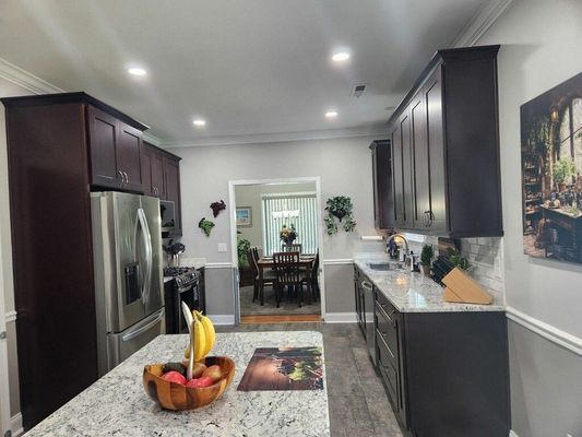 Kitchen with dark cabinets, stainless steel appliances, granite countertops, and an island with fruit.
