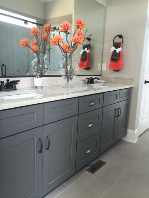 Gray vanity with dual sinks, gray cabinets, granite countertop, orange flowers, and matching orange towels.