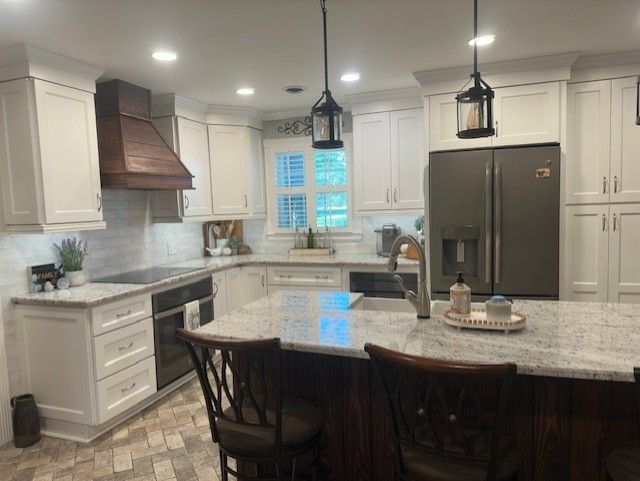 White kitchen with a wood range hood, stainless steel appliances, and a granite island.