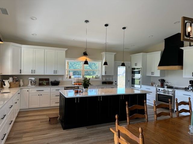 Spacious kitchen with white cabinets, black island, three pendant lights, and wooden dining table.