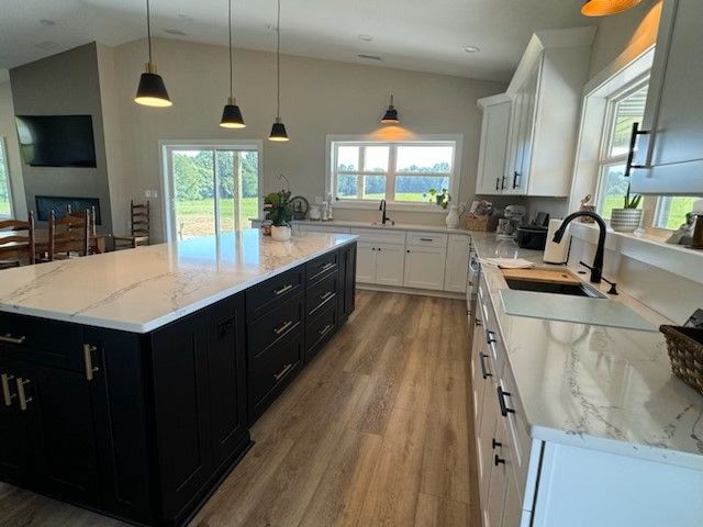 Spacious modern kitchen with black island, white countertops, and wood-look flooring. Natural light floods the space.