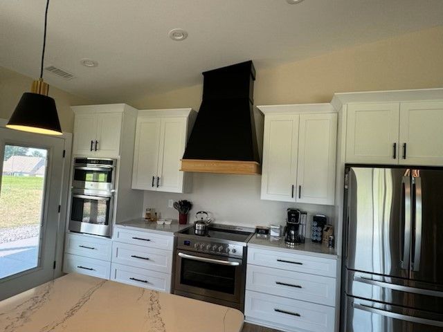 White kitchen cabinets surround a black range hood above a stainless steel stove.