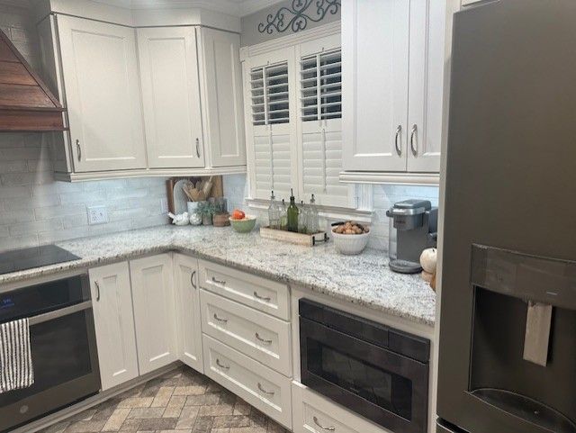 White kitchen with granite countertops, white cabinets, and stainless steel appliances.