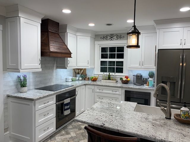 White kitchen with a wooden range hood, light granite countertops, and stainless steel appliances.