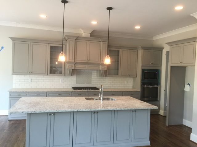 Gray kitchen with island, cabinets, and two pendant lights. White backsplash, granite countertops, and dark flooring.