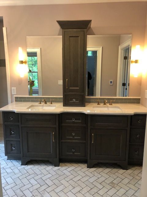 Bathroom vanity with dark gray cabinets, marble countertop, gold fixtures, and herringbone floor.