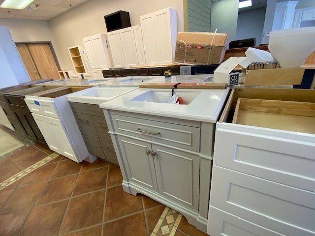 Bathroom vanity cabinets displayed in a showroom. Various styles, colors (white, gray, brown), and sizes.