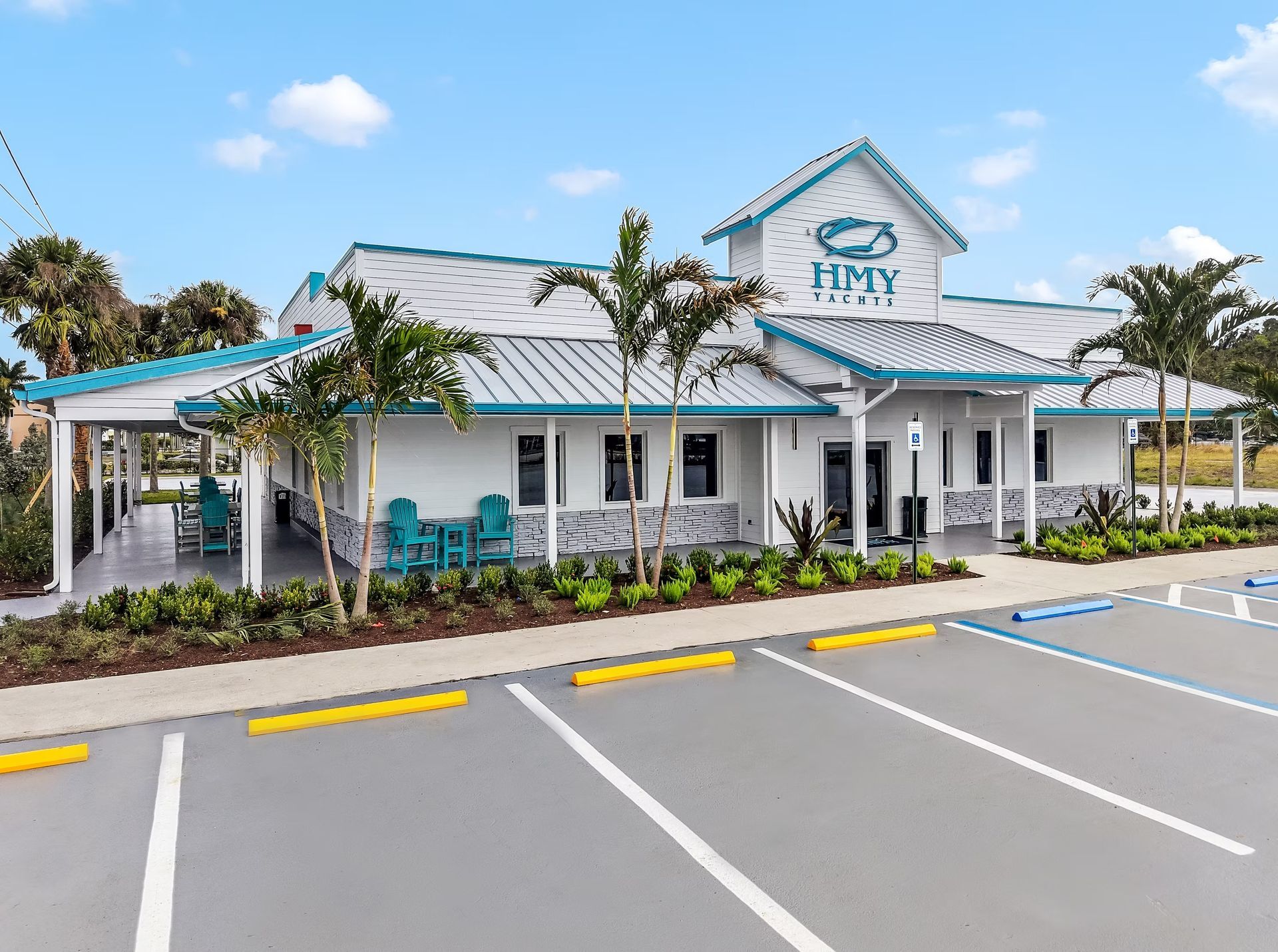 Small white building with teal roof and porch, seen from an empty parking lot on a sunny day