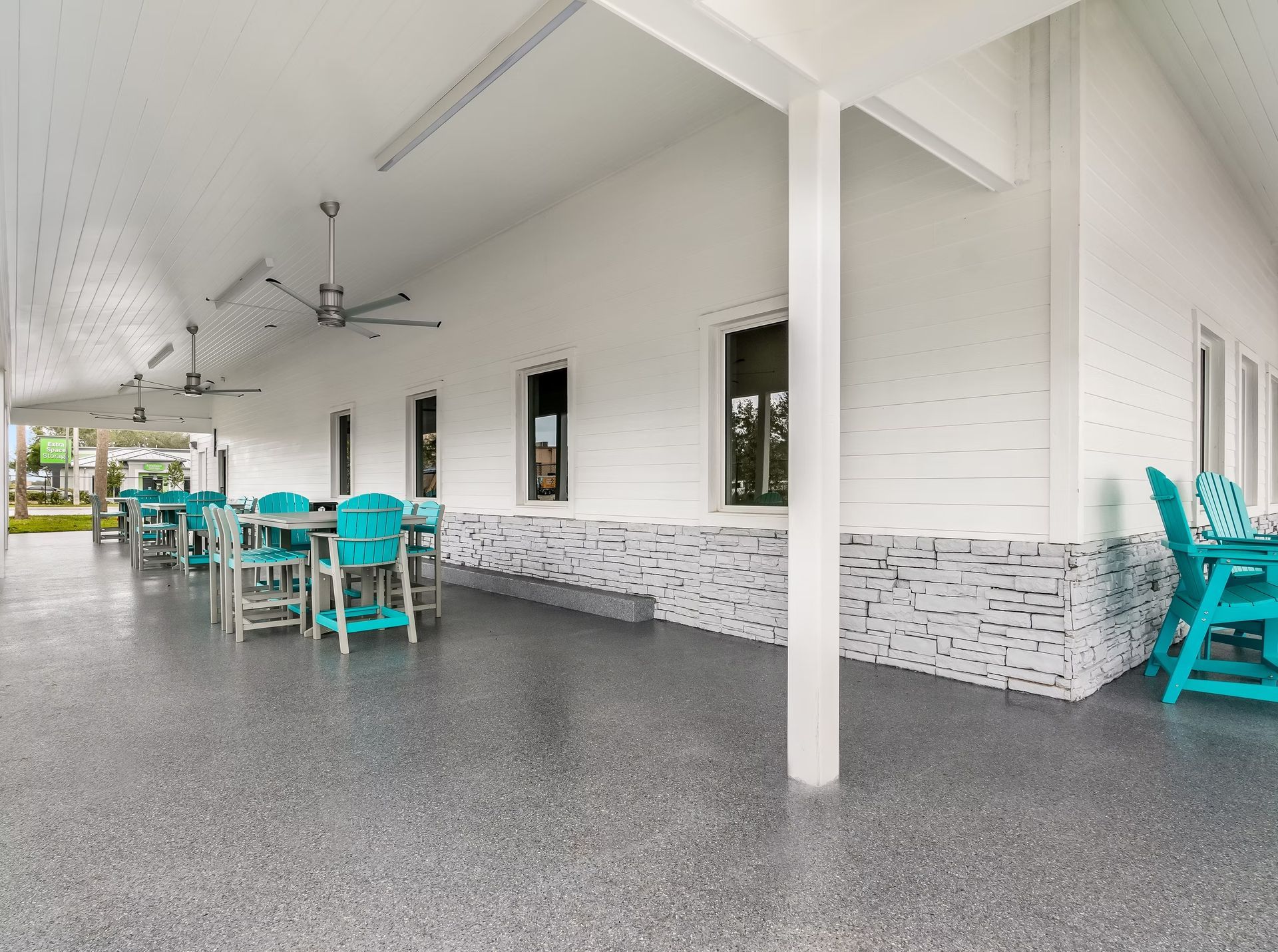 Covered outdoor patio with turquoise chairs and tables beside a white building