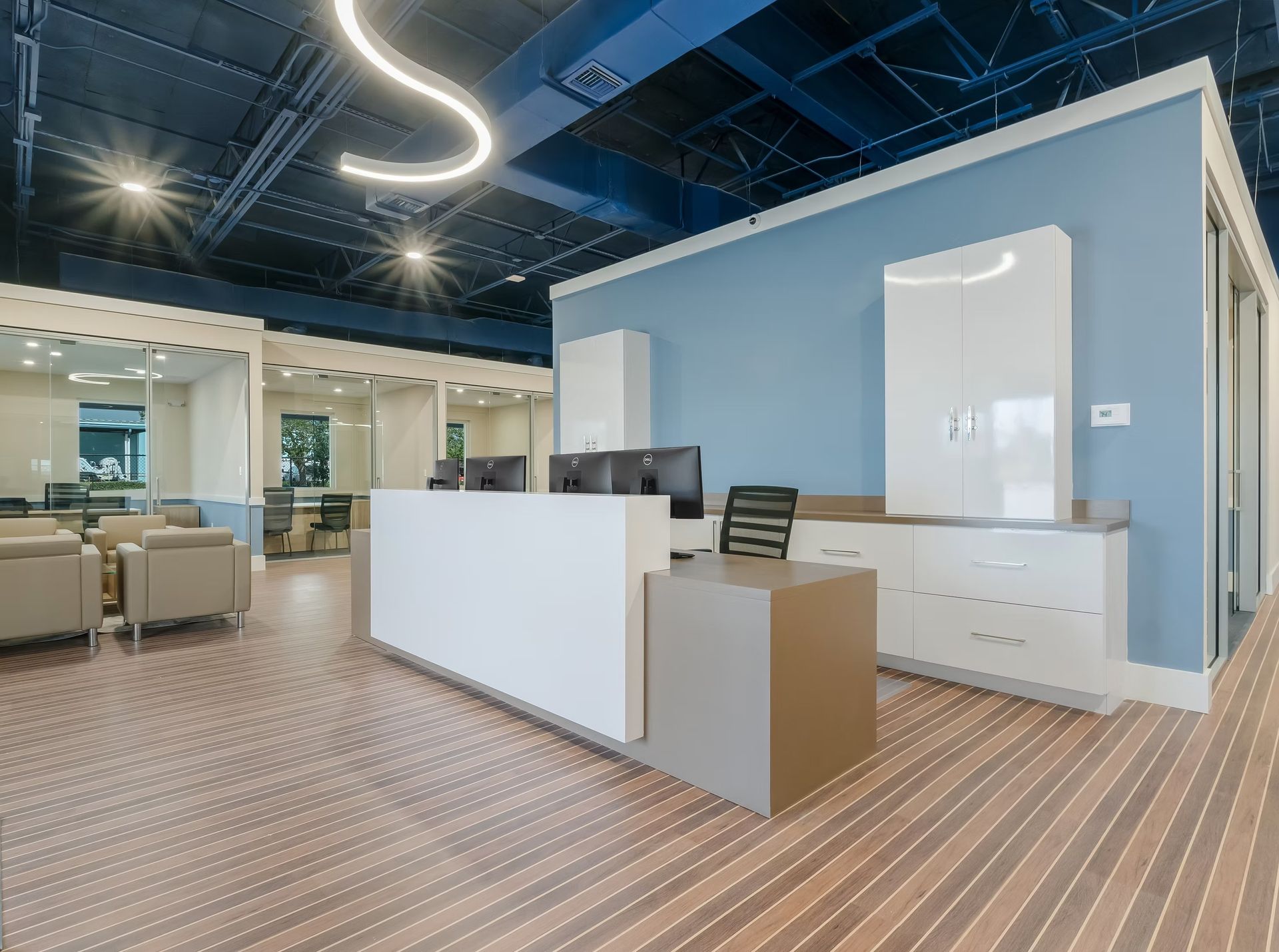Modern office reception area with white desk, beige cabinets, and blue walls under bright ceiling lights