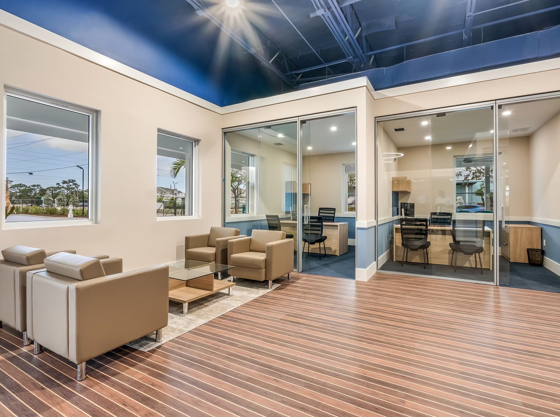 Modern lounge with beige chairs, glass walls, patterned floor, and blue ceiling lights