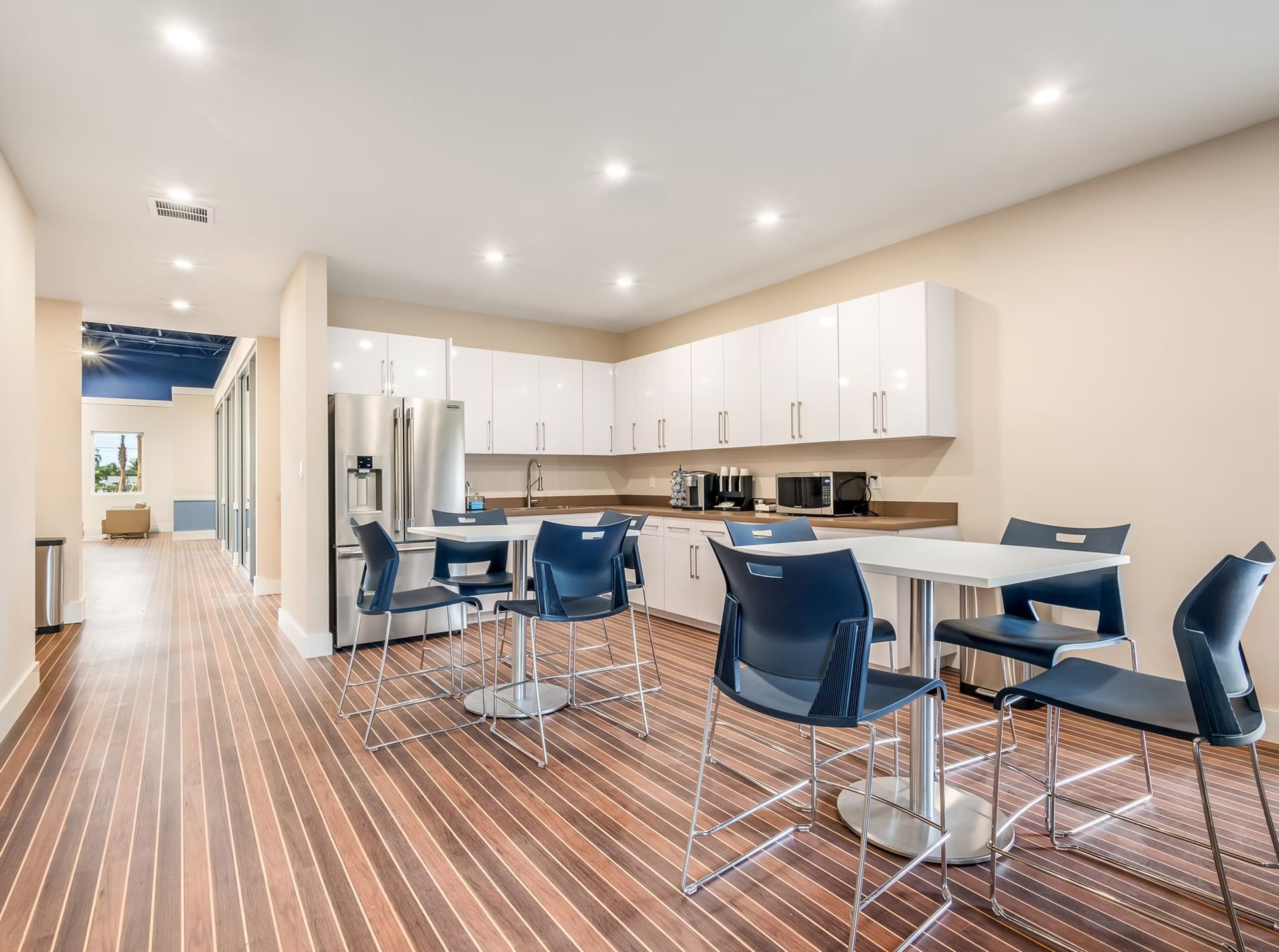 Bright modern kitchen with white cabinets, stainless appliances, and blue bar stools on wood flooring