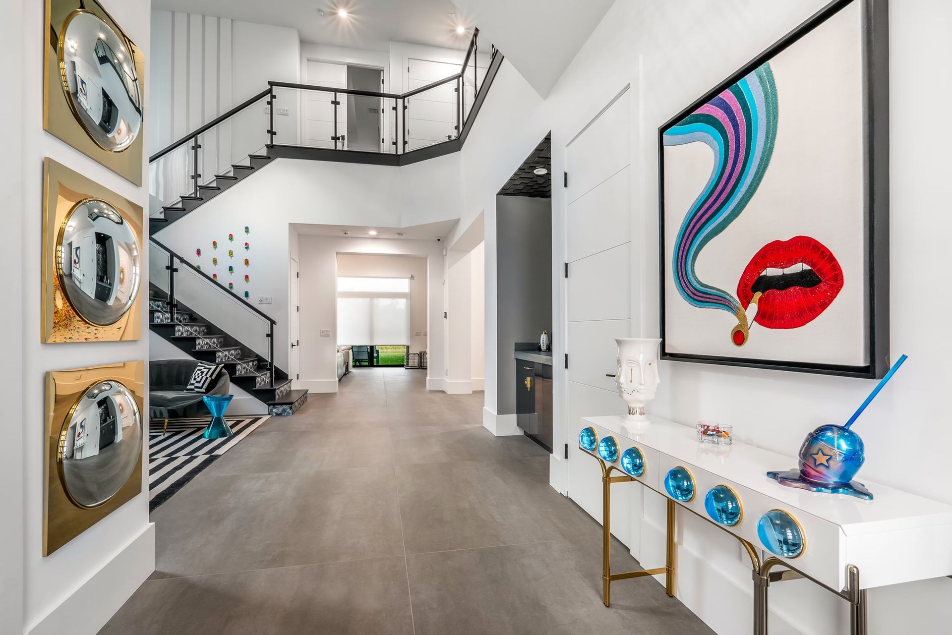 Modern white foyer with staircase, large abstract lips artwork, and metallic decor accents