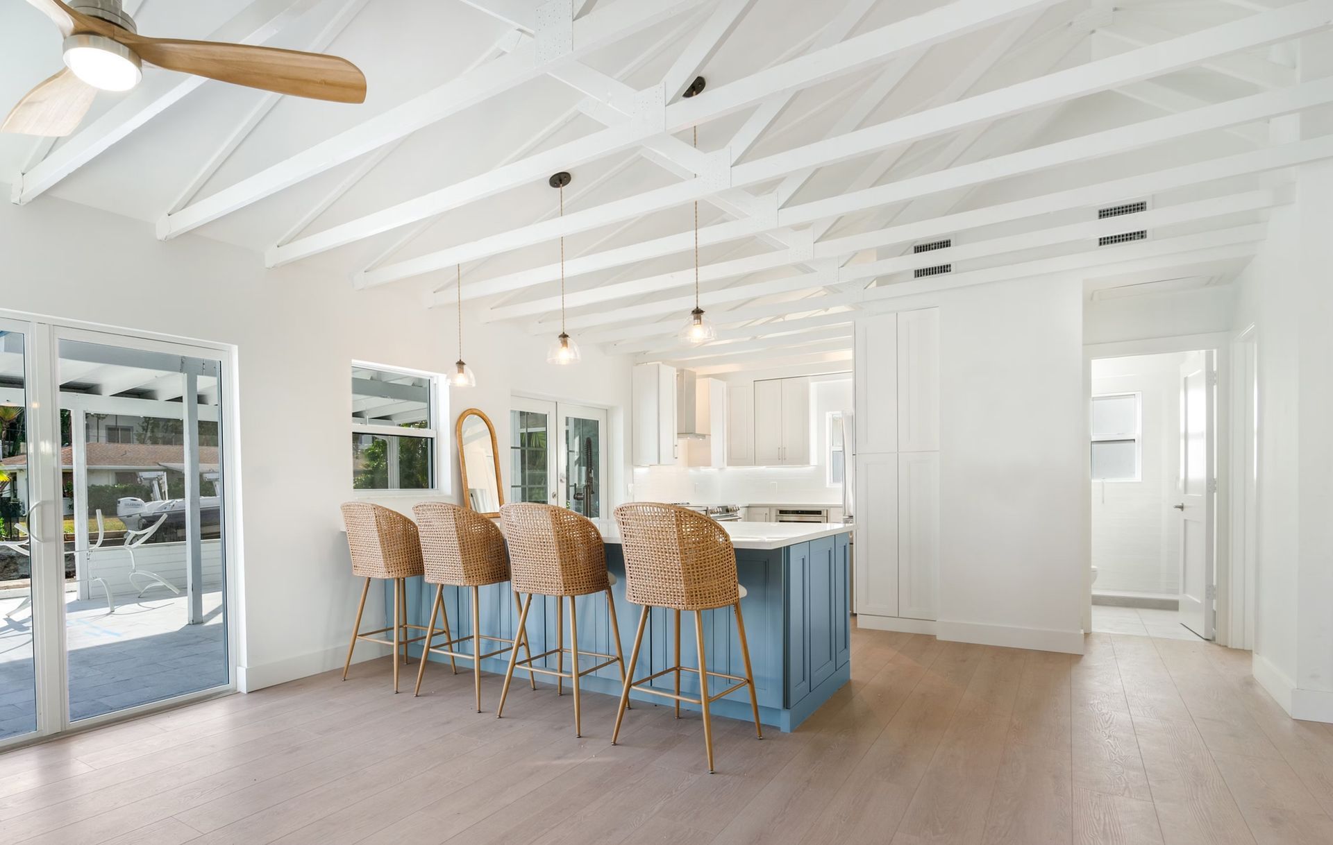 Bright white kitchen with blue island, woven bar stools, vaulted ceiling, and sliding glass doors
